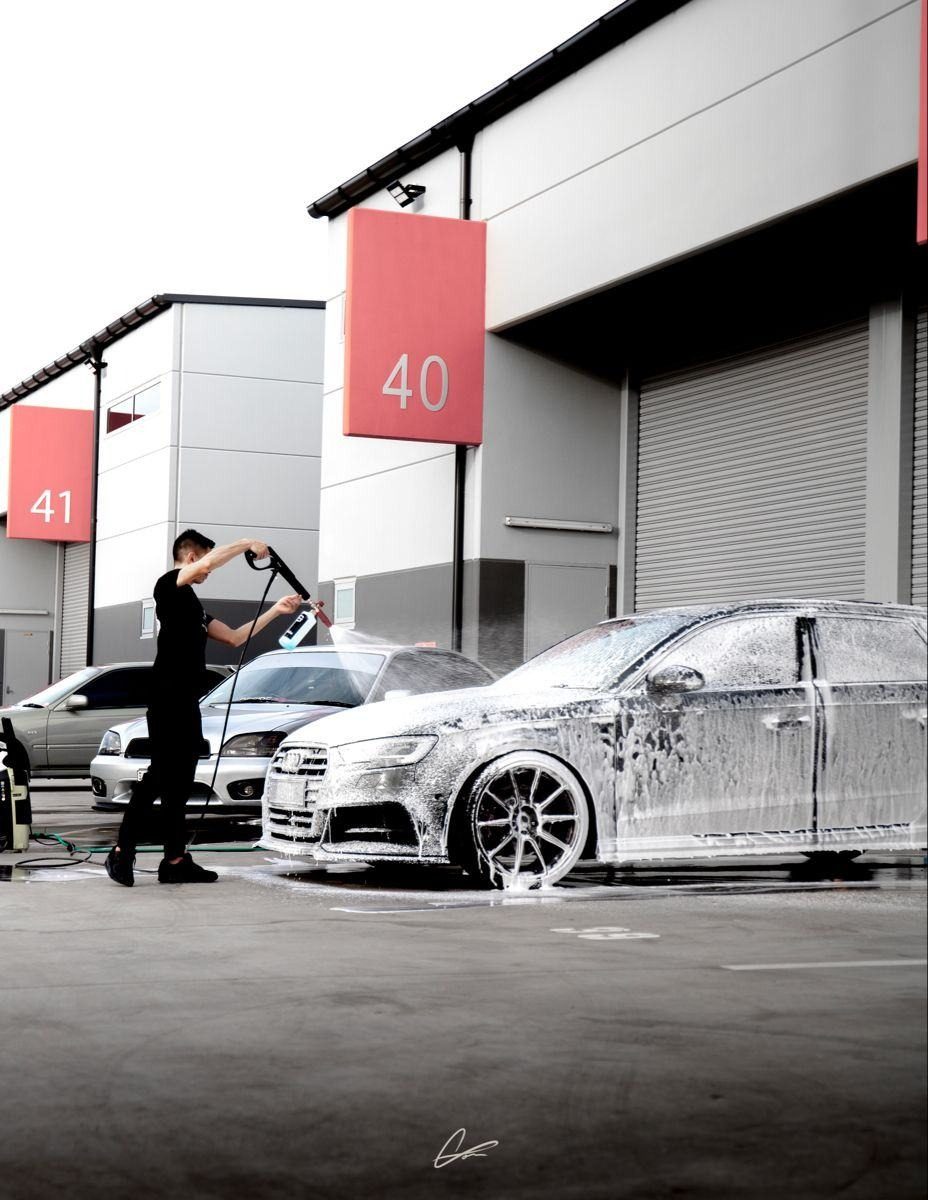 Technician foaming a hatchback outside a car wash bay