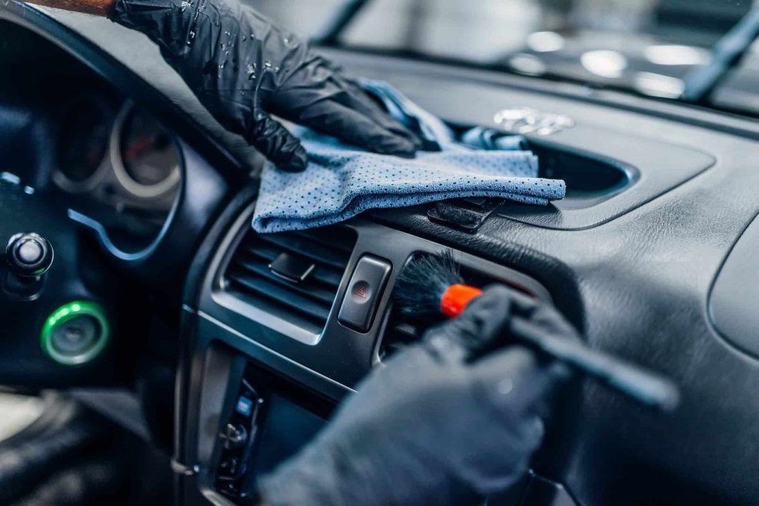 Technician cleaning a car dashboard with a microfiber cloth and brush